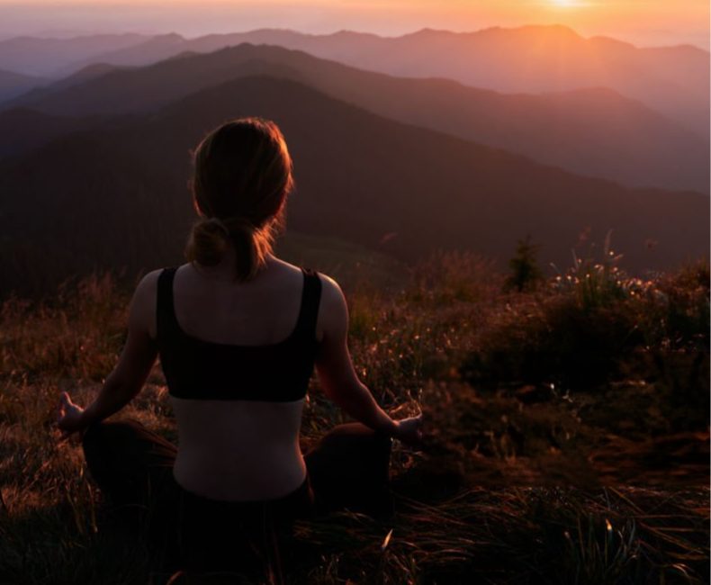 A practitioner meditating at sunrise above the mountains